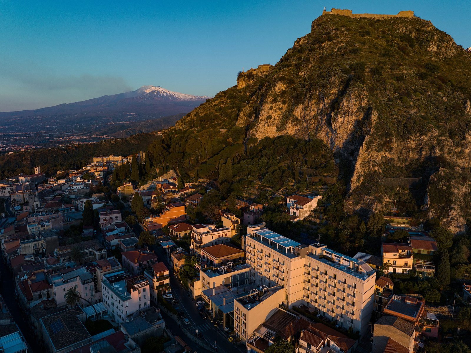 Taormina seen from the air at sunset, with Mount Etna smoking on the horizon